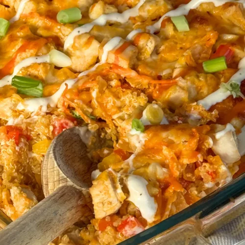 A baked buffalo chicken quinoa casserole drizzled with green onions and ranch dressing with a wooden spoon digging into it.