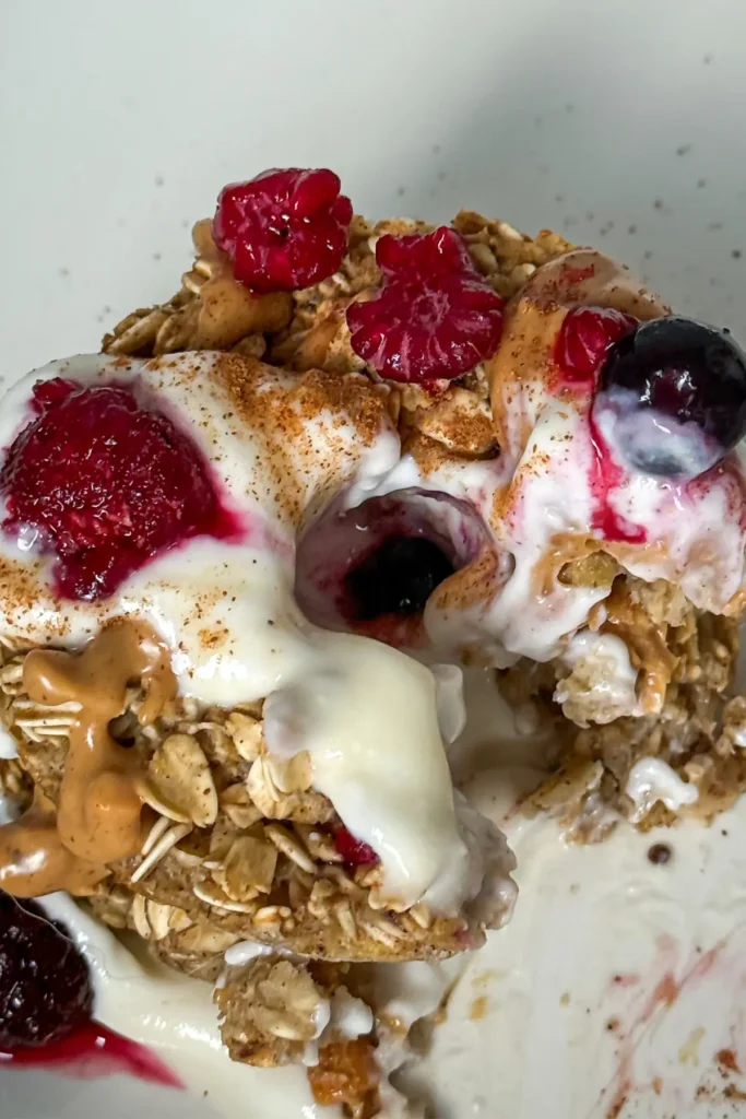 Two baked oatmeal donuts topped with Greek yogurt and berries with some bites taken out of it.