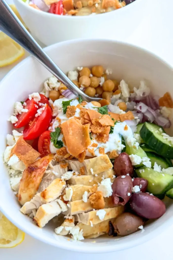 A Greek chicken bowl topped with garlic Greek yogurt and crushed pita chips on a counter.