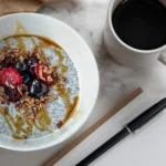 A chia breakfast bowl next to a cup of coffee and a piece of paper with a pen on a counter.