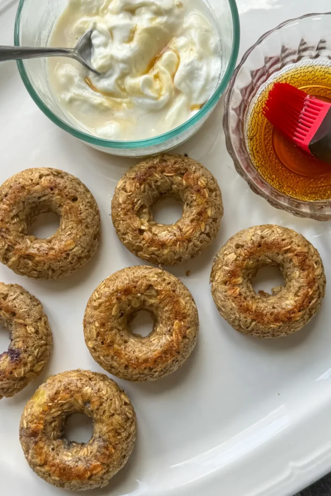 A birds-eye view of cooled baked donuts next to a bowl of yogurt and a bowl of syrup on a platter.