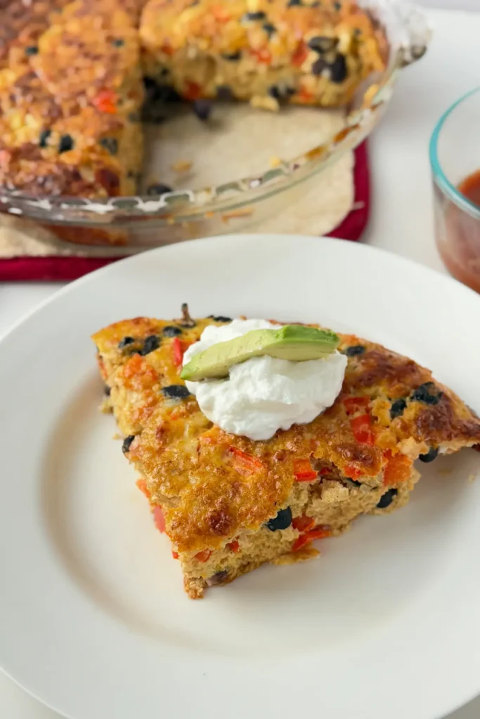 A slice of quinoa breakfast baked topped with Greek yogurt and avocado on a plate next to a baking dish of it.