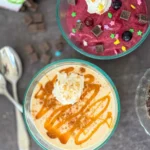 A birds-eye view of two bowls of soft serve; one with frozen banana and caramel and the other frozen berries with dark chocolate chips and whipped cream.