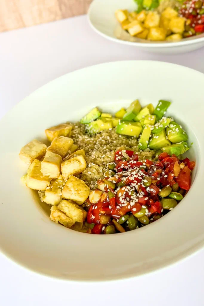 A tofu, quinoa, edamame bowl on a table next to another bowl.