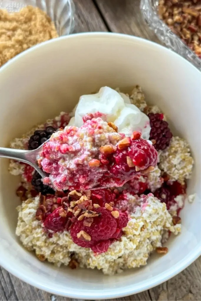 Coconut milk quino mixed in a bowl with berries and whipped cream with a close-up on a spoonful.