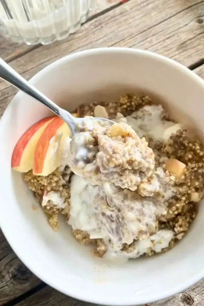 A bowl of nutty quinoa with diced apples and Greek yogurt mixed in with a spoon of it in focus.