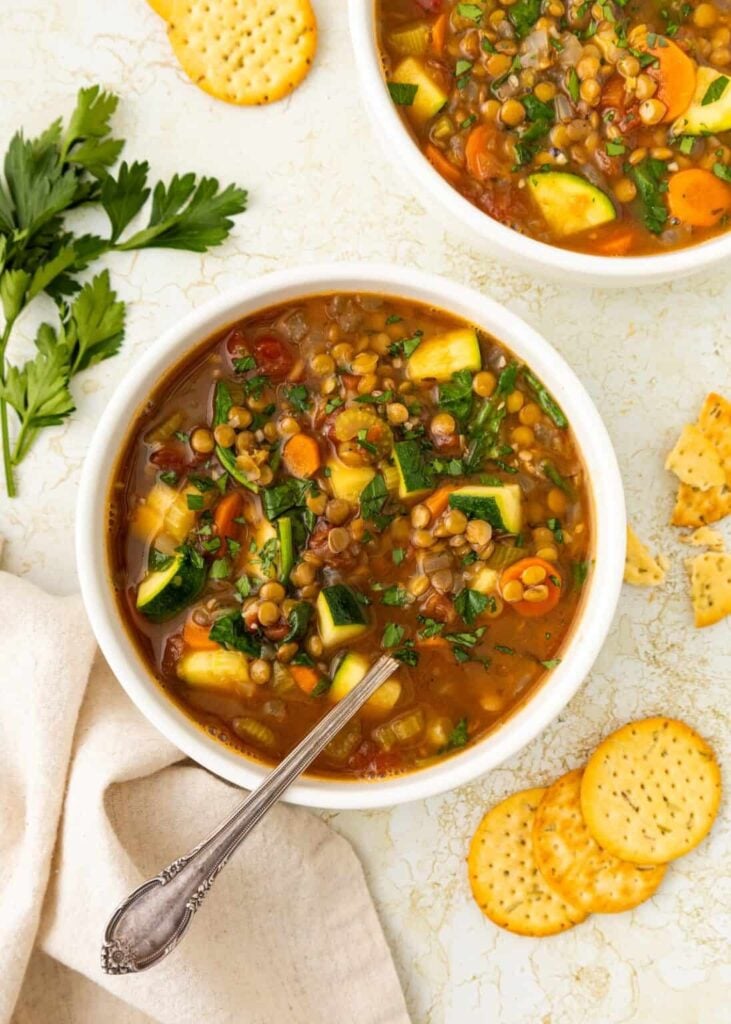 A birds-eye view of two bowls of veggie-packed lentil soup on a table next to crackers.