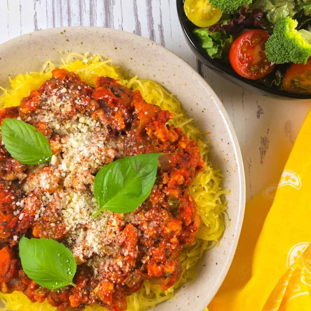 Spaghetti squash in a bowl topped with a tempeh bolognese sauce and parmesan cheese on a table.