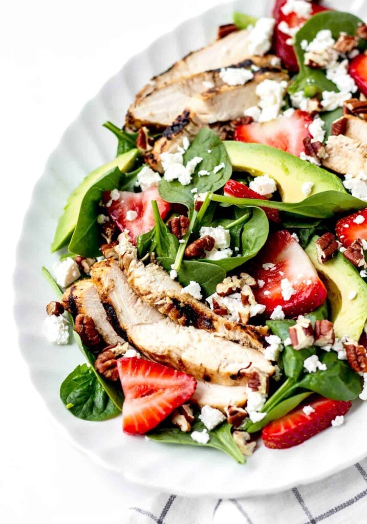 A strawberry and grilled chicken salad on a white platter.