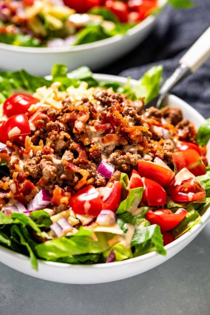 A close-up of a bowl of cheeseburger salad with a fork in it on a table.
