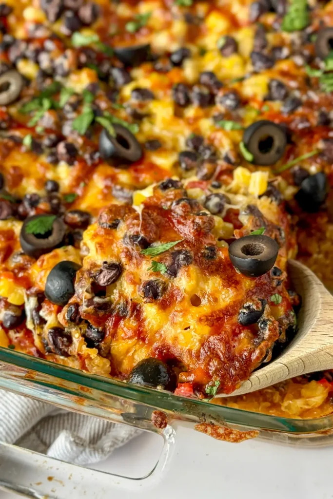 A close-up of a wooden spoon digging into a baked Mexican casserole with quinoa on the counter.