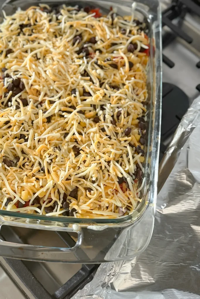 The cooked quinoa casserole on a stove with shredded cheese sprinkled on it.