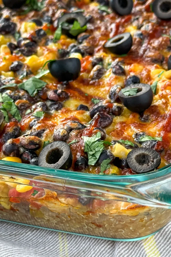 A close-up of a baked one pan casserole with quinoa topped with black olives and cilantro on a counter.