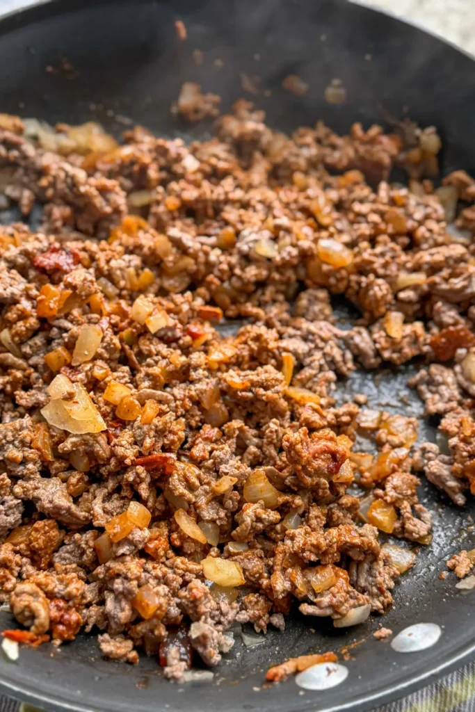 A close-up of a pan of cooked ground beef with taco seasoning and cooked onions.