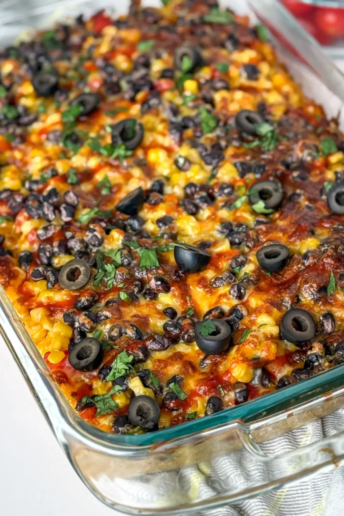 A baked quinoa casserole in a casserole dish with hot sauce drizzled on top and olives.