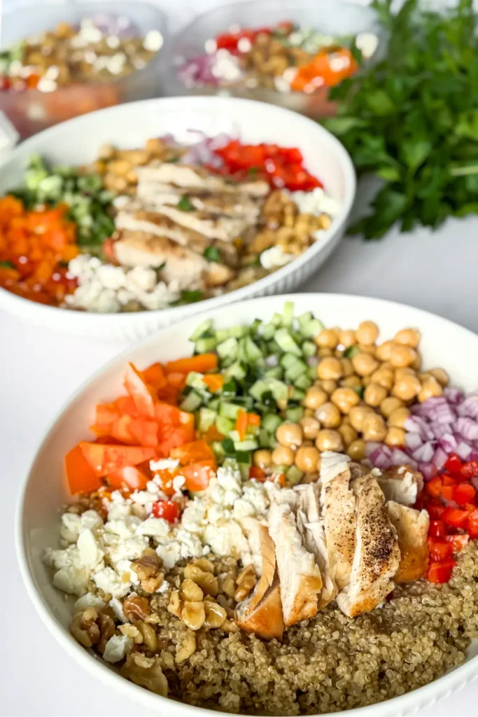 Two fully assembled Mediterranean chicken and veggie bowls with chickpeas and quinoa on a counter.