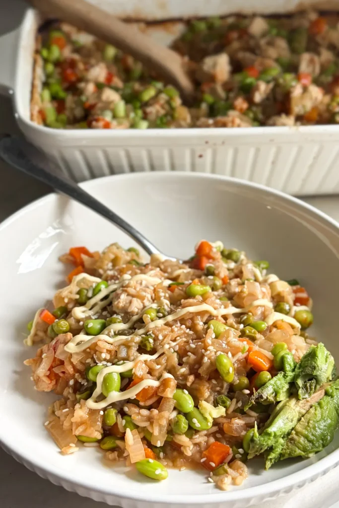 A plated chicken fried rice casserole next to the casserole dish on a counter.