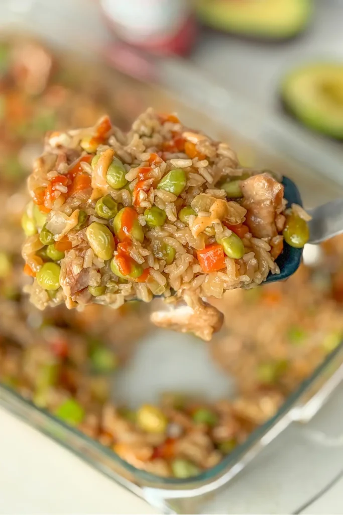 A close-up of a big spoonful of chicken fried rice over the casserole dish on a table.