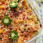 A birds-eye view of a baked street corn casserole on a decorative towel on the counter next to limes.