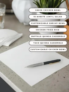 A piece of pen and a paper on a counter in the kitchen with text on the screen listing the 7 easy dinner ideas for this meal plan.