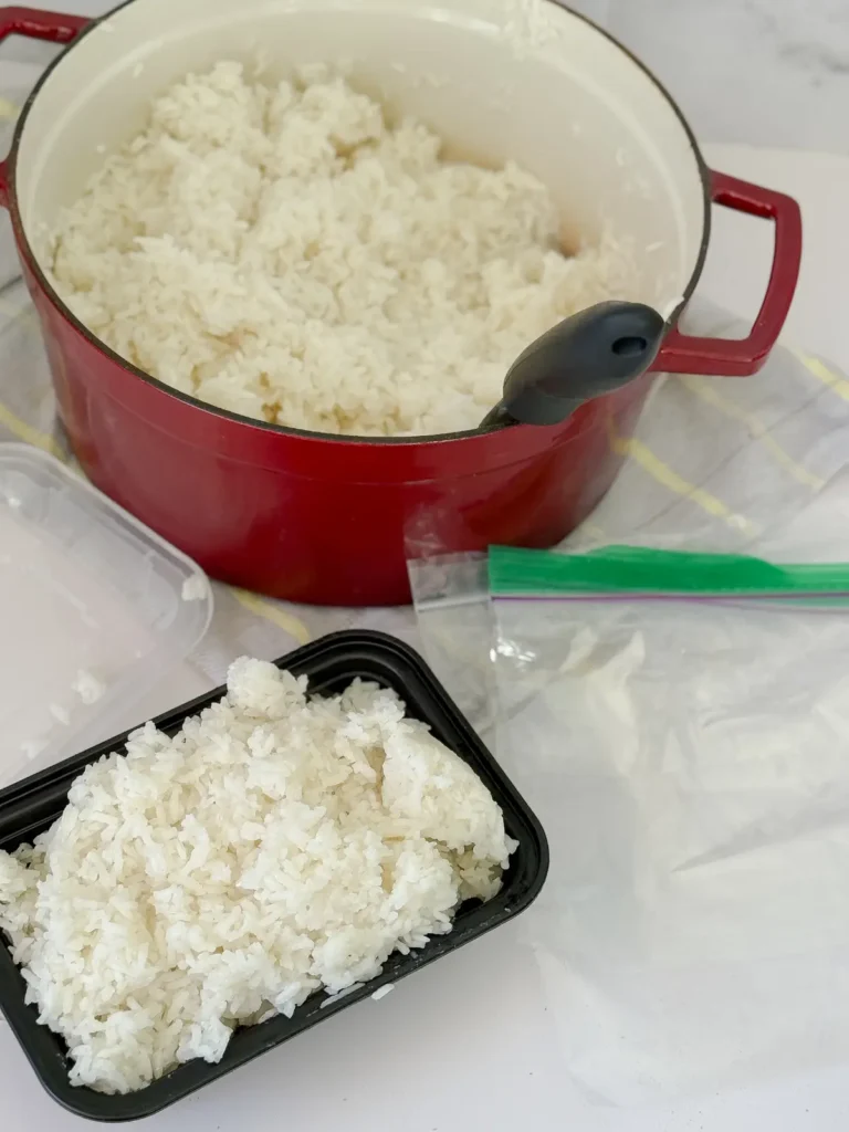 A big pot of rice on a counter next to a storage container of rice and small zip-loc bags.