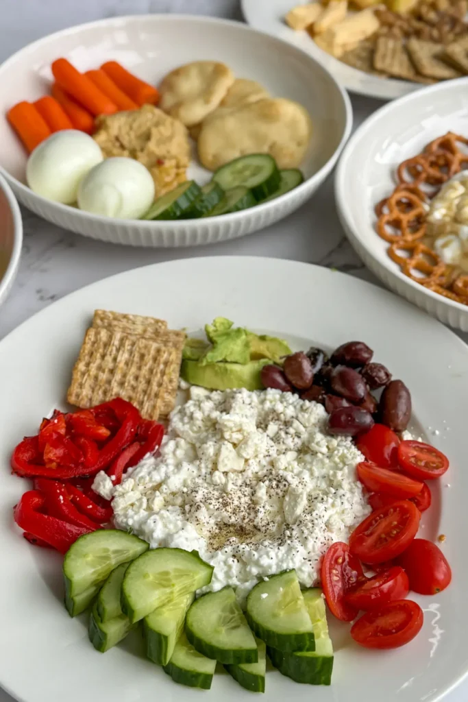 A Mediterranean savory cottage cheese plate next to the rest of the snack plates on a counter.