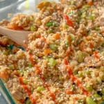 A wooden spoon digging into a chicken fried rice casserole after baking.