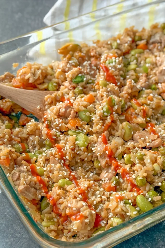 A wooden spoon digging into a chicken fried rice casserole after baking.