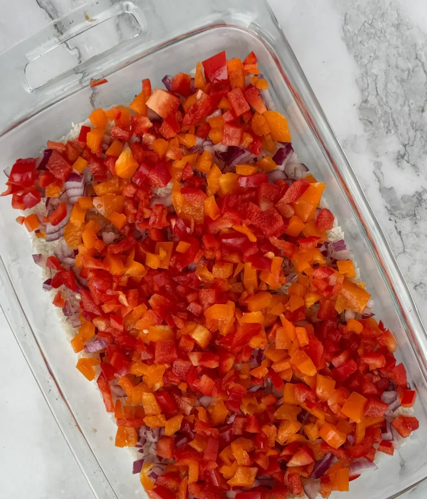 Rice, diced onion, and peppers in a casserole dish prior to baking.