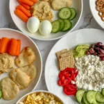 A birds-eye view of different snack plates and a bowl of popcorn sprinkled with nutritional yeast on a counter.
