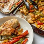 Barbecue chicken and veggies on a plate next to two large sheet pans with chicken and veggies on them.