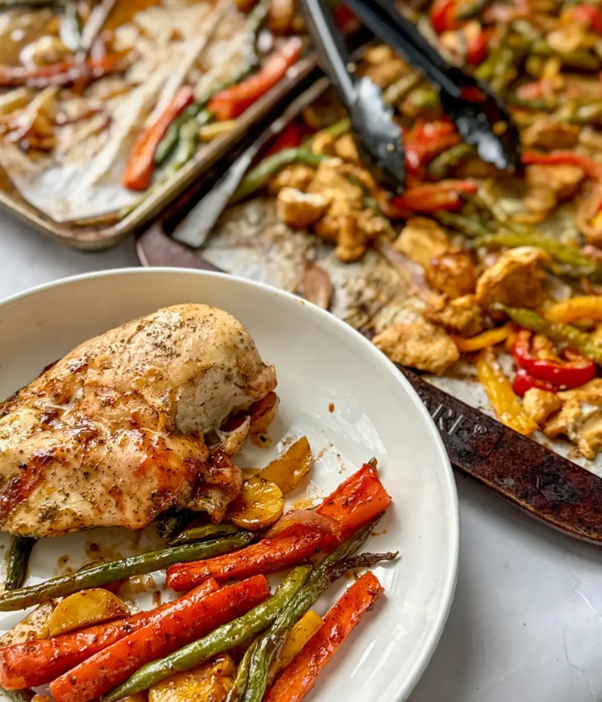 Barbecue chicken and veggies on a plate next to two large sheet pans with chicken and veggies on them.
