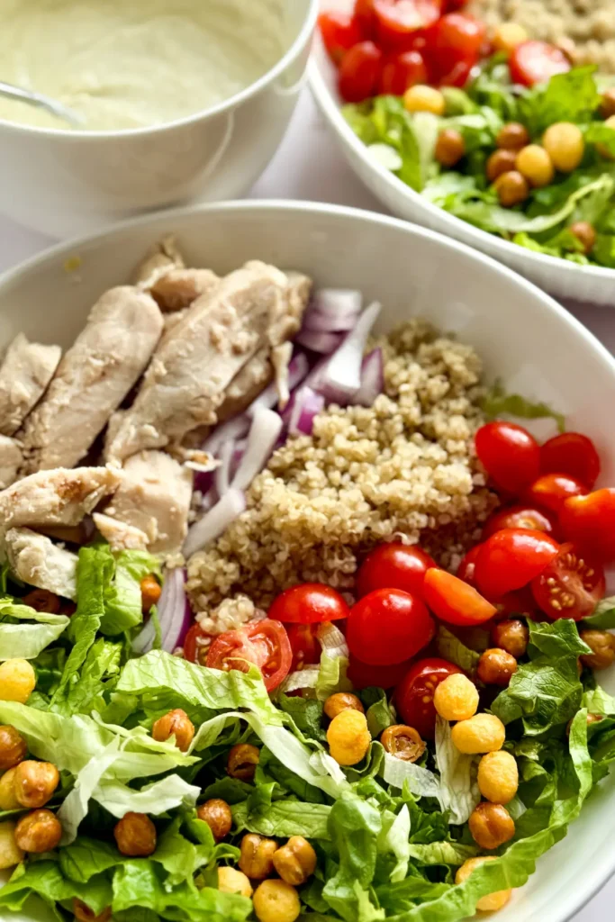 Two fully assembled bowls next to a large bowl of yogurt Caesar dressing.