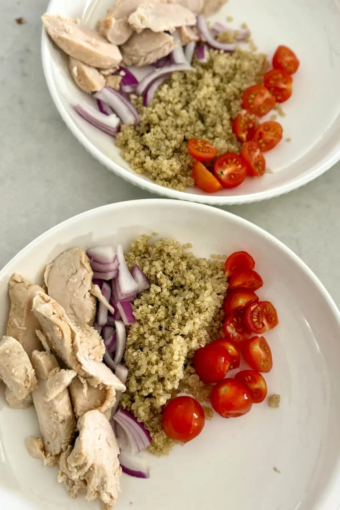 Two bowls with quinoa, cherry tomatoes and chicken on them.