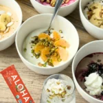 Yogurt bowls next to a protein bar and a smoothie on a counter.
