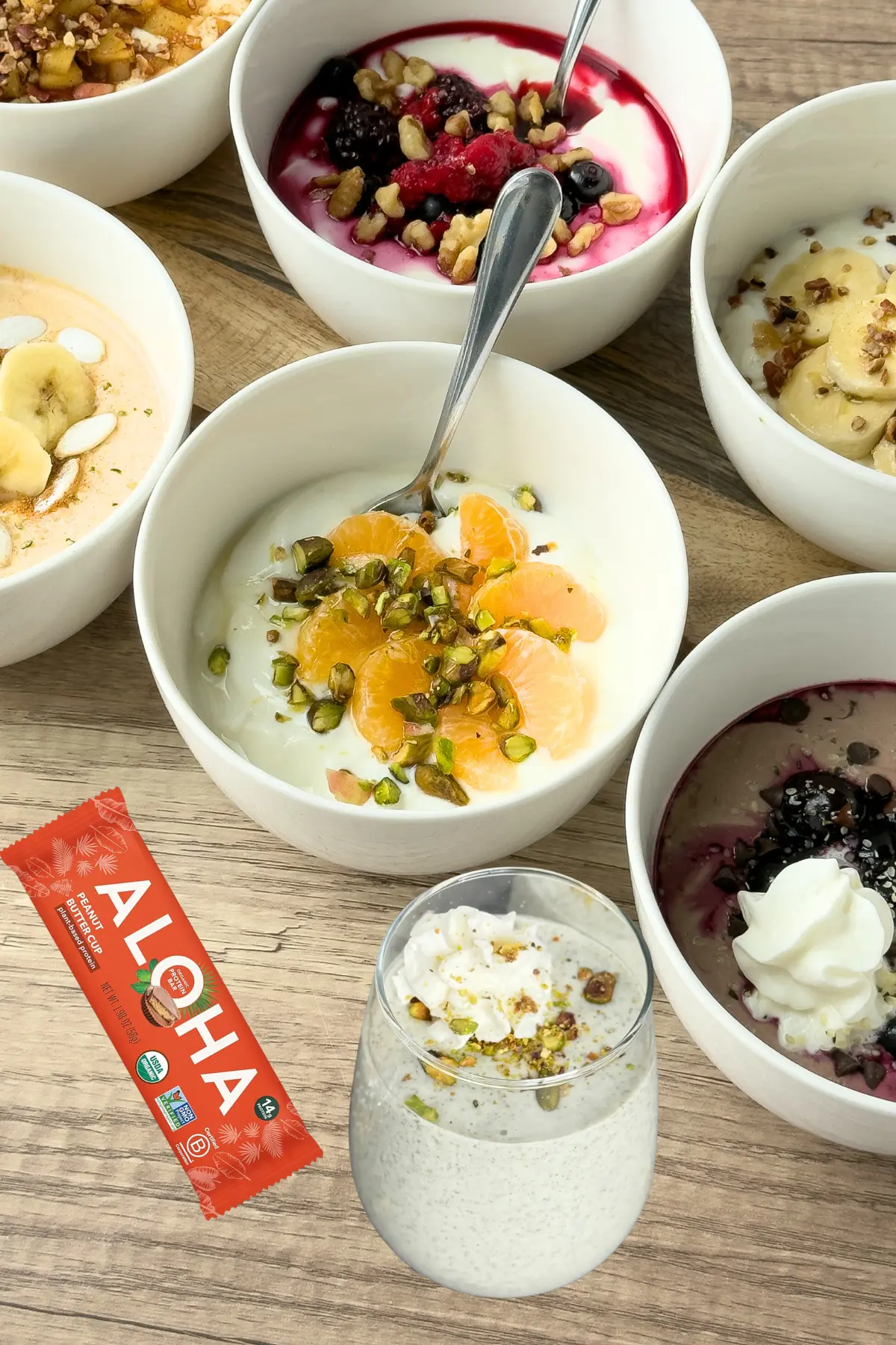 Yogurt bowls next to a protein bar and a smoothie on a counter.