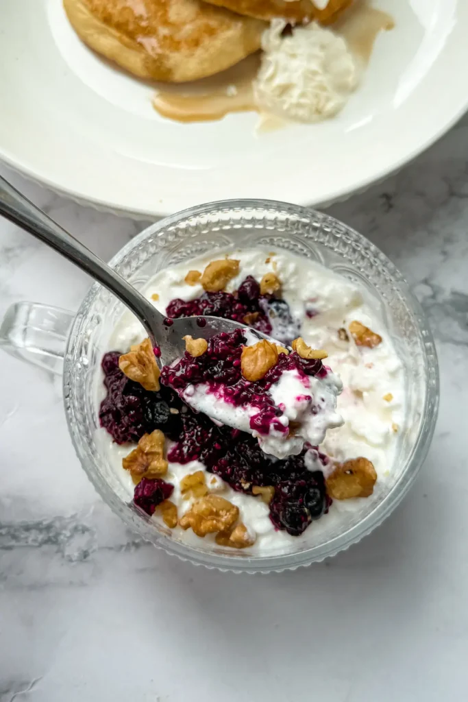 A birds-eye view of a cottage cheese bowl topped with chia seed jam and nuts with a spoon in it on a table.
