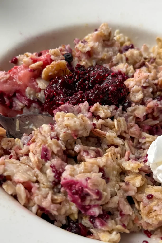 A close-up of a bowl of oatmeal with chia seed jam and a dollop of whipped cream on it.