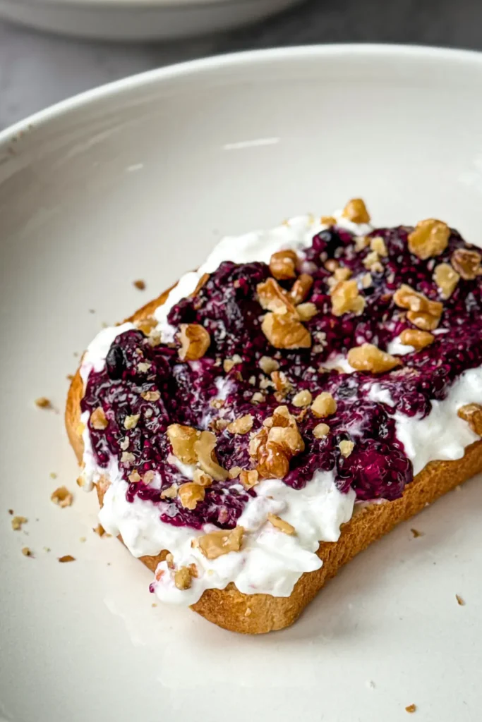 A slice of bread with a layer of cottage cheese and a layer of chia seed jam on a white plate.