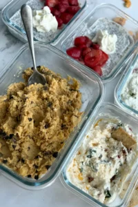 A counter full of snack prepped items like chickpea cookie dough, cottage cheese dips and chia pudding.
