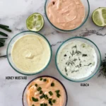 Four different Greek yogurt sauces in small glass containers on a counter.