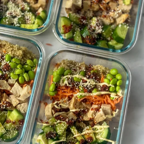 A birds-eye view of four meal prep storage containers with Asian chicken and quinoa on a counter.