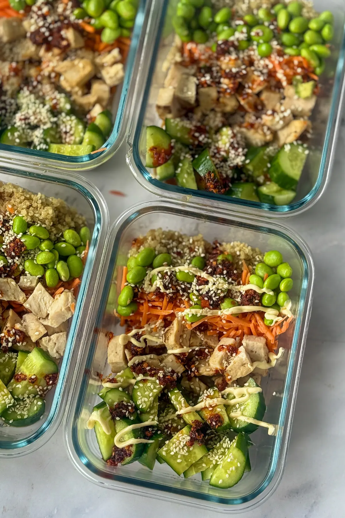 A birds-eye view of four meal prep storage containers with Asian chicken and quinoa on a counter.