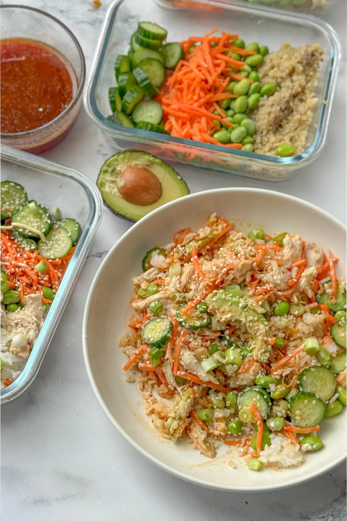 An avocado chicken and rice bowl next to assembled meal prep containers, half an avocado, and the sauce in a glass bowl.