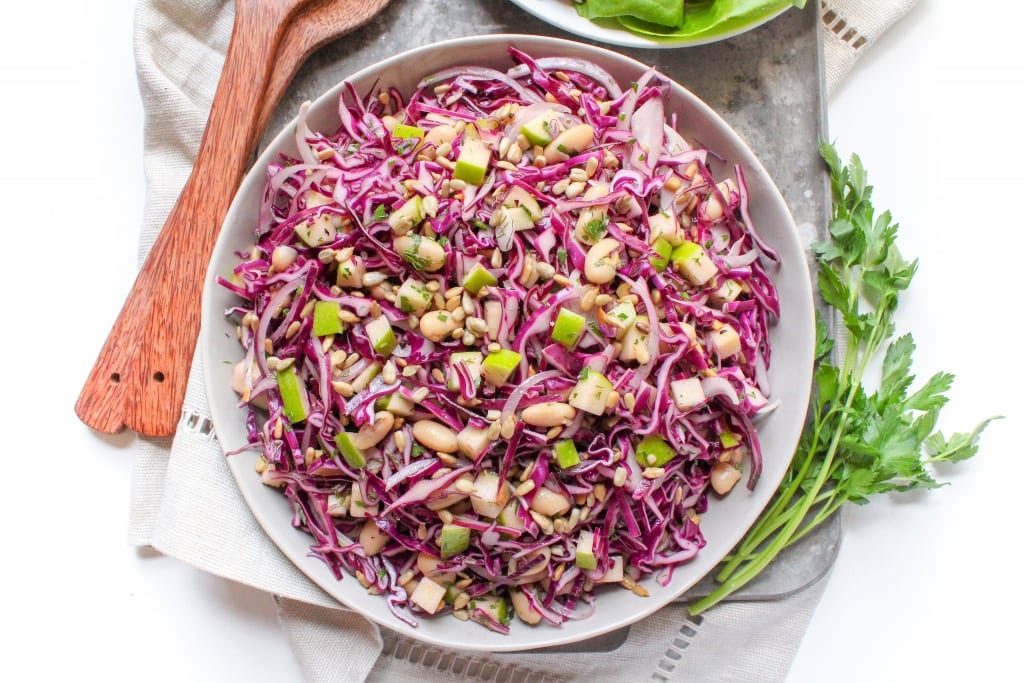 A big bowl of cabbage slaw on a table next to a wooden spoon.
