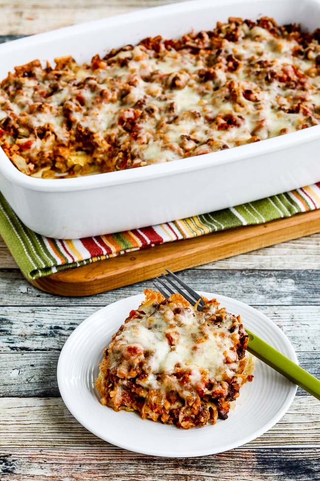 A slice of cabbage casserole on a plate next to a large casserole dish on a table. 