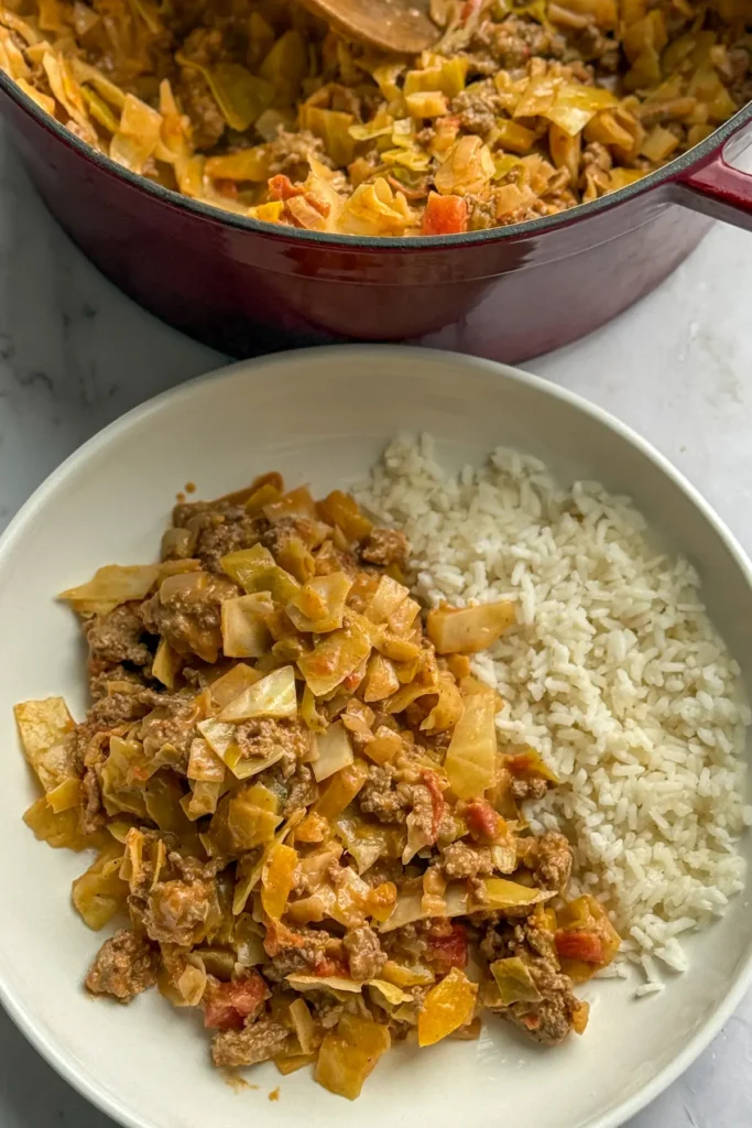Ground beef and cabbage stir-fry on a plate with rice next to a huge pot of it on a table.