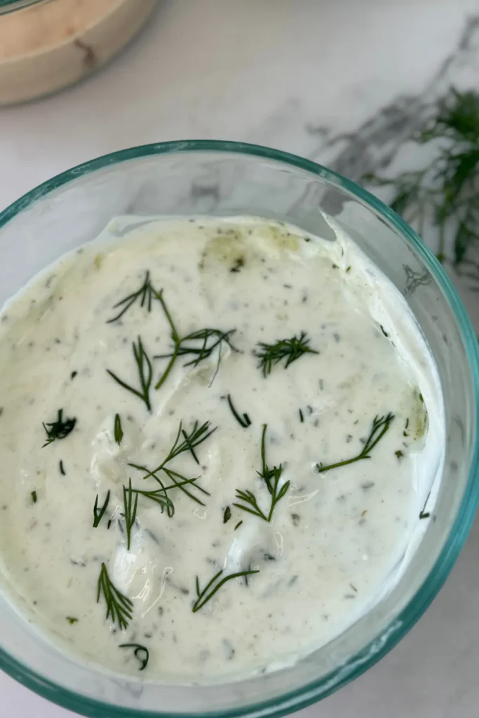 A bowl of Greek yogurt ranch garnished with dill on a counter.