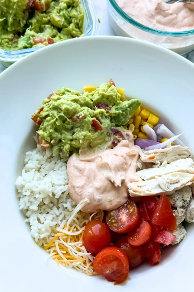 A Mexican-inspired power bowl with rice, veggies and chicken topped with the chipotle adobo sauce next to a container of guacamole and a the Greek yogurt sauce.