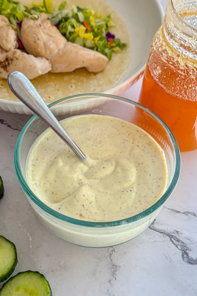 A bowl of honey mustard next to an open-faced chicken wrap and a glass of honey.